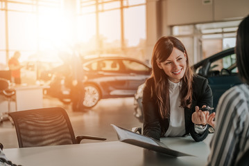 Happy saleswoman with folder giving car key to new owner.