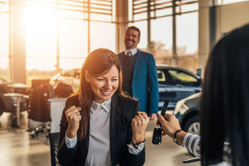 Smiling woman receives the keys to a new car from a sales manager.