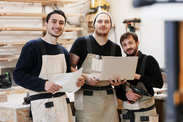 Master of small business with laptop and his team as sign of innovation in carpenter workshop. startup business, young specialist