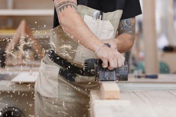 Carpenter working with electric planer on wooden plank in workshop. Hands and planer close up....