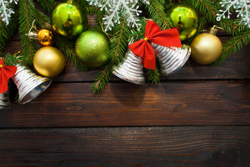 Green living spruce branches on a dark wooden background. New Year background with beautiful balls and white snow and bells. Top view