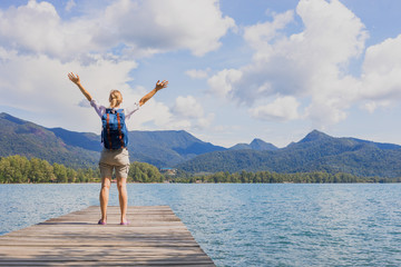 Happy female traveler with backpack raising arms, tropical travel destination