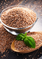 Bowl of uncooked spelt on wooden table