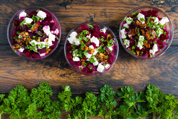 Healthy beet salad with cheese, parsley, walnuts and Greek yogurt in small glass bowls on the rustic wooden table, top view.