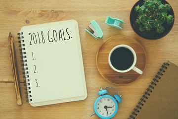 Top view 2018 goals list with notebook, cup of coffee on wooden desk.