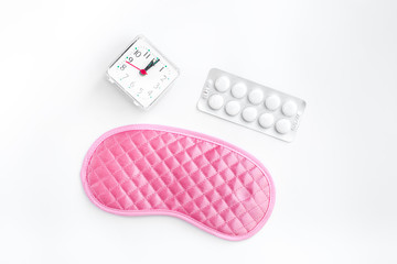Sleeping pills for insomnia near sleep mask and alarm clock on white background top view