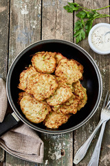 Zucchini fritters in a frying pan and yogurt sauce, top view. Healthy, vegetarian food