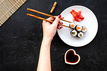 Hand takes sushi roll with salmon and avocado with chopstick. Black background top view