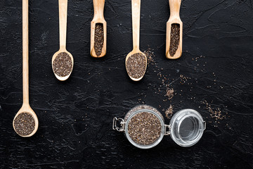 Superfood chia seeds in a wooden spoon and scoop on black background top view copyspace