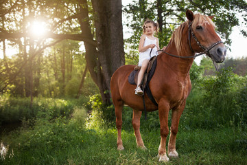 Obraz premium Llittle girl is riding a horse. Summer meadow.