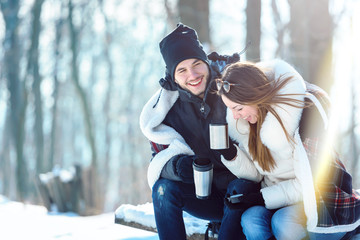 Smiling young couple with cups sititng in snow covered mountain forrest