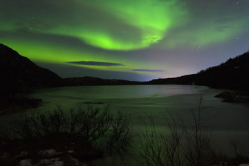 The Aurora in the night sky over hills and a frozen lake.