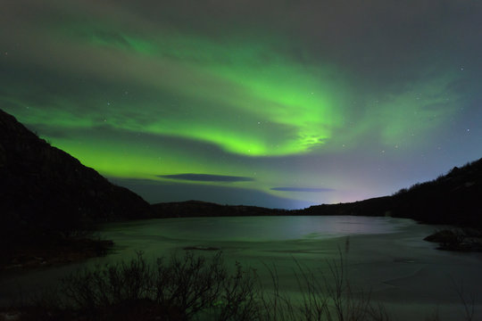 The Aurora in the night sky over hills and a frozen lake.