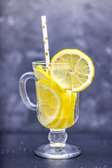 Homemade lemonade in a glass with a handle on a gray concrete background. Water with slices of lemon on a dark background.
