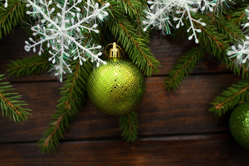 Green living spruce branches on a dark wooden background. New Year background with green balls and white snowflakes. Top view