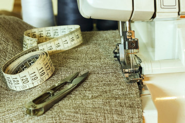 The foot of the overlock close-up, near the fabric, centimeter and scissors.