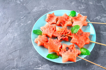 Watermelon in the form of stars on skewers with leaves of mint lies on a plate. The blue dish is like a rocket in space. Top view.