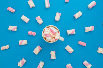 Cappuccino mug with marshmallows on blue background. Flat lay, top view