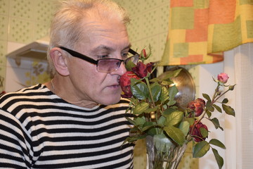 пожилой человек наслаждается ароматом роз,им выращенных на загородном  саду   