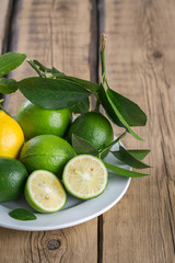lemon and limes with leaves on a white plate on a wooden background