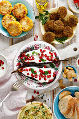 Grilled aubergine with yoghurt sauce, pomegranate seeds and fresh herbs on a ceramic plate and other tasty vegetarian snacks, top view. Concept of delicious and healthy meal