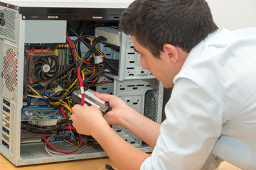 Young technician working on broken computer in his office