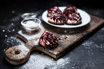 small desserts with different stuffings, sprinkled with berry topping, sprinkled with powdered sugar on a white plate on a wooden board on a dark background