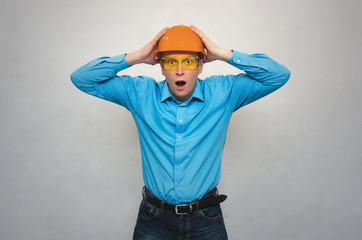 Confused builder worker with open mouth holding a head with his hands and in shocked from from what happened. Accident in production or construction. Stress situation.