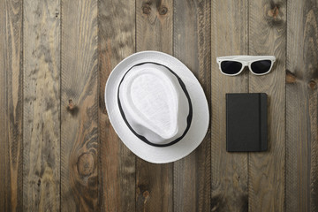 Sombrero blanco, gafas de sol y libreta sobre fondo de madera, vistos desde arriba