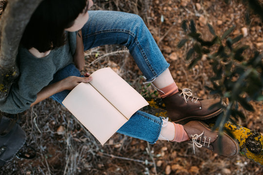 Soft focus shot of cute and beautiful young woman or girl student resting during hike or walk in park. Wears blue denim jeans, pink socks and brown leather boots, read book or notebook diary mockup