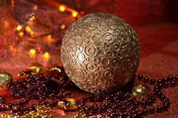 Big golden ball with ornaments among red and golden Christmas decoration composed of stars, jingles and strings of pearls