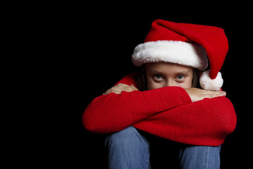 Merry Christmas. The young girl in a red sweater and Santa's cap is resting on her hands and smiling.