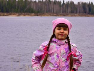 Cheerful girl with pigtails on the river bank at the beginning of winter
