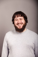 A happy man with a beard and dark hair, dressed in gray