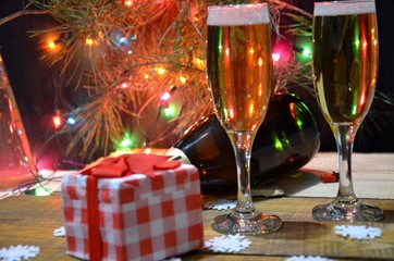 two glasses of champagne on the background of champagne. Christmas tree with Christmas lights. New Year and Christmas. Gift boxes tied with bows