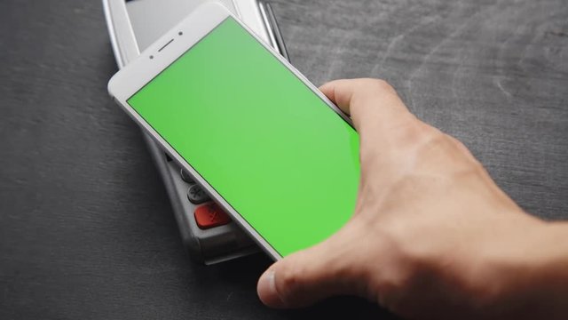 Top view of person using contactless payment with smartphone. Green screen template on phone.