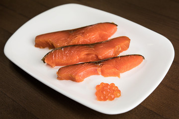 three slices of red fish and caviar on a white plate