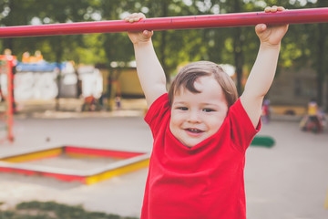 Fototapeta premium portrait of cute little boy in red t-shirt excitedly playing and smiling on playground. concept of happy healthy child