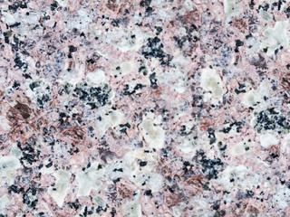 A close-up of a surface of treated rose granite rock plate. A fragment of a stone wall decoration. Texture of red granite facing material.