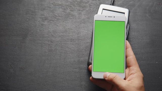 Top view of person using contactless payment with smartphone. Green screen template on phone.