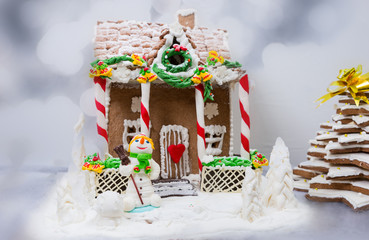 Gingerbread house, gingerbread Christmas tree and a sugar mastic snowman on background of defocused silver lights