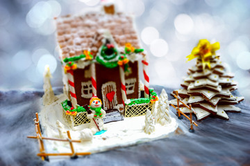 Homemade gingerbread house, gingerbread Christmas tree and a sugar mastic snowman on background of defocused silver lights