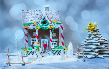 Gingerbread house and Christmas tree near a sugar mastic snowman on background of defocused silver lights as a snow