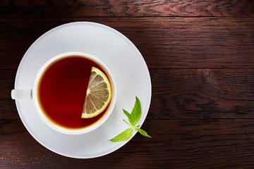 Tea with lemon in white cup, cinnamon sticks, knitted woolen scarf on wooden table