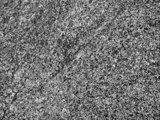 A close-up of a surface of polished grey granite rock plate. A fragment of a stone wall decoration. Texture of black-and-white granite facing material.