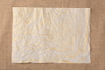 Old crumpled paper sheet on canvas sackcloth background. Top view.