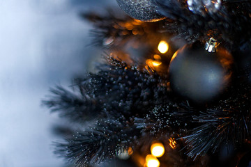 Christmas dark blurred background with a black Christmas tree, ornaments and bokeh lights