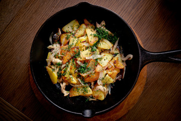 Fried potatoes with herbs dill and onion in a frying pan on wooden table. Top view.