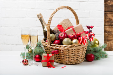 Two glasses of champagne with Christmas basket with bottle, gifts with red satin ribbon, candy...