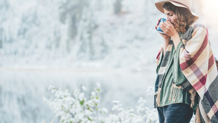 Pretty woman drinking hot coffee and enjoying vacations among stunning winter landscape. Traveling in mountains wilderness. Wanderlust and boho style